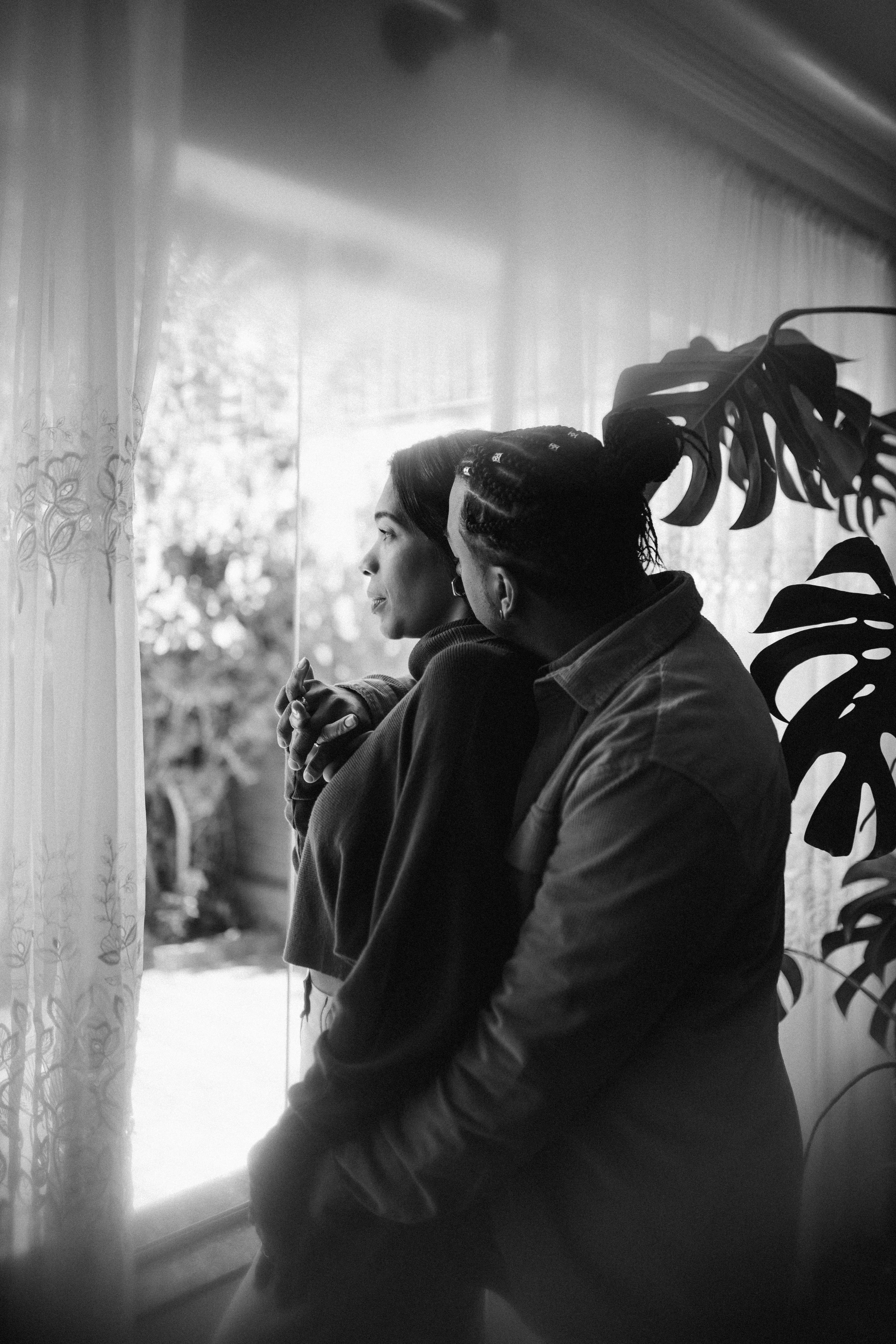 Fotografia em preto e branco de Erik abraçando Paula junto à janela.