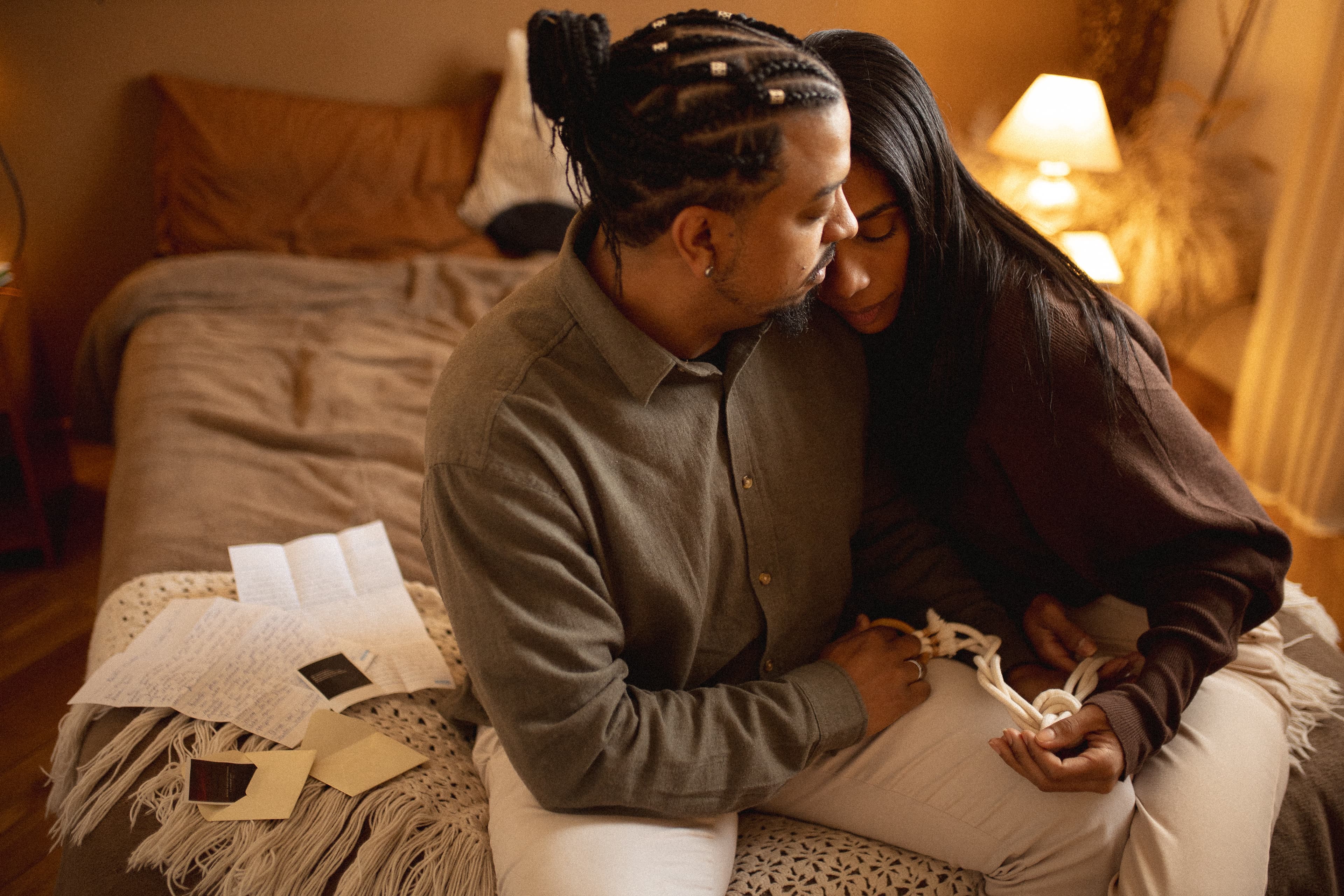 Paula e Erik se abraçam na cama, com cartas e lembranças ao lado.